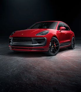 2026 Porsche Cayenne Turbo Electric prototype wrapped in neon test-livery under studio lighting with a wireless charging pad beneath it.
