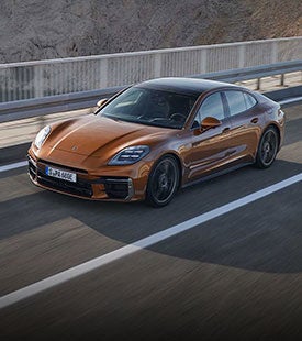 2026 Porsche Cayenne Turbo Electric prototype wrapped in neon test-livery under studio lighting with a wireless charging pad beneath it.