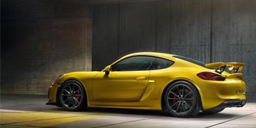 2026 Porsche Cayenne Turbo Electric prototype wrapped in neon test-livery under studio lighting with a wireless charging pad beneath it.