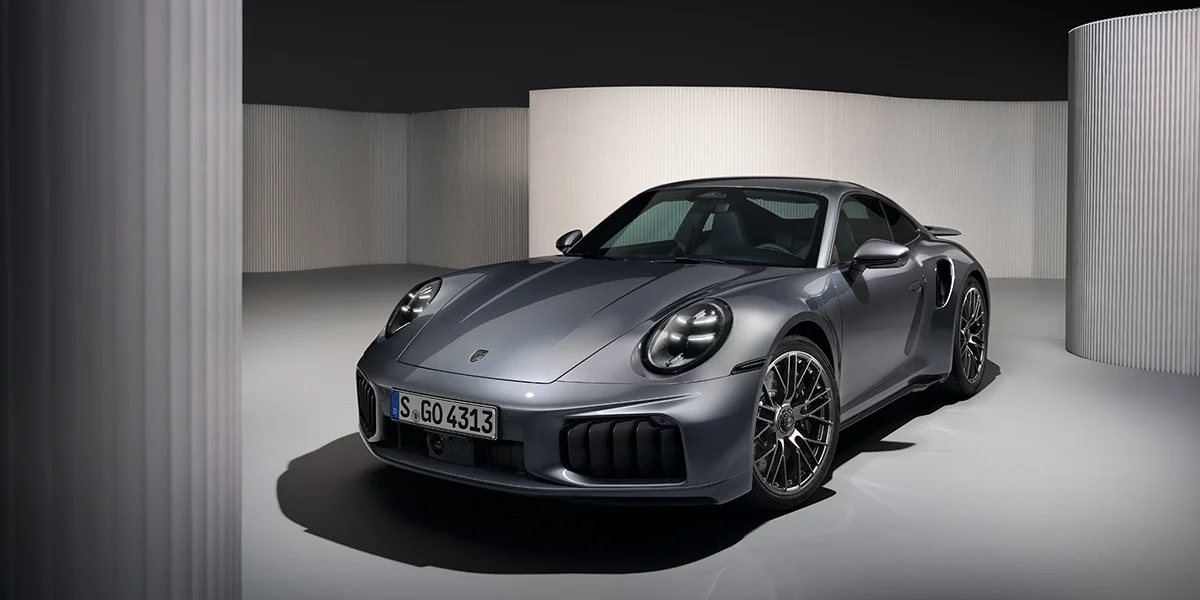 Front three-quarter view of Porsche 911 Turbo S in Agate Grey metallic, emphasizing aggressive front fascia and wide body design.