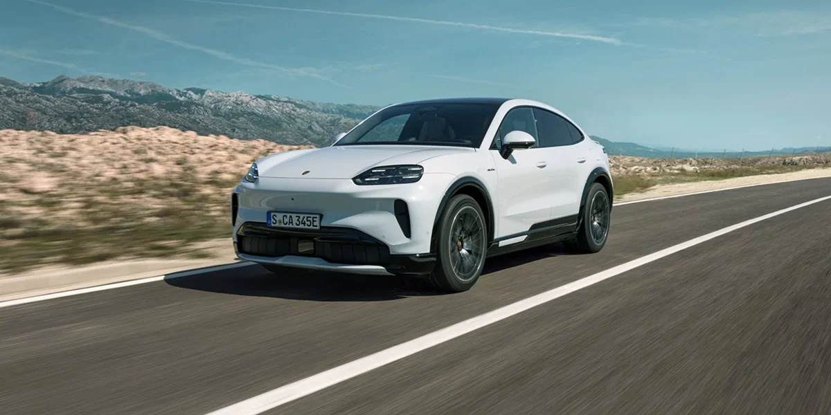 2026 Porsche Cayenne Turbo Electric prototype wrapped in neon test-livery under studio lighting with a wireless charging pad beneath it.