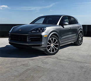 2026 Porsche Cayenne Turbo Electric prototype wrapped in neon test-livery under studio lighting with a wireless charging pad beneath it.